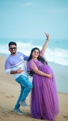 a man and woman standing on top of a sandy beach next to the ocean with their arms in the air