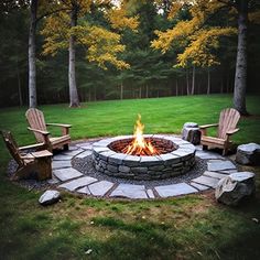 a fire pit surrounded by chairs in the middle of a grassy area with trees and grass