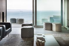 a living room filled with lots of furniture next to a large glass window overlooking the ocean