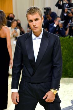 a man in a tuxedo is posing for the camera while people are taking pictures behind him