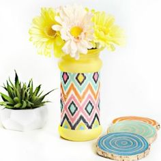 a yellow vase with flowers and coasters on a white surface next to a potted plant