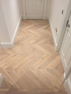 an empty hallway with wooden floors and white walls, leading to another room that has two doors