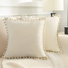 three white pillows with pom - poms on them