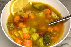 a bowl of soup with carrots, broccoli and lemon