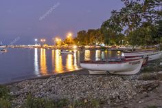 two boats on the shore at night with lights reflecting in the water and trees around them