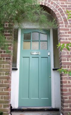 a green door is in between two brick pillars and an arch over the front door