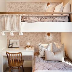 a bedroom with two bunk beds and a desk in front of the bed has pillows on it