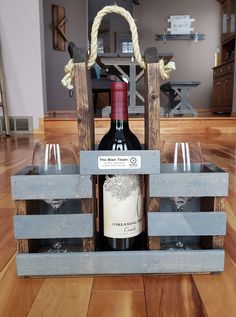 a wine bottle and two glasses in a wooden crate with rope on the top, sitting on a wood floor