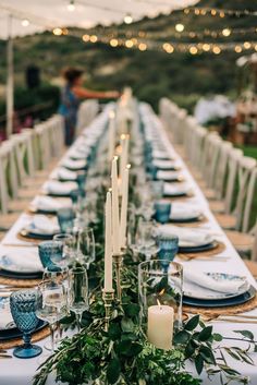 a long table is set with candles, plates and greenery for an outdoor dinner