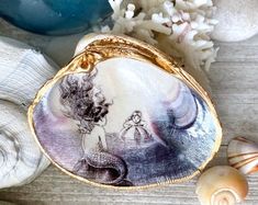 a shell with an image of a mermaid on it next to seashells