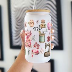 a hand holding a white mason jar with sewing related images on it