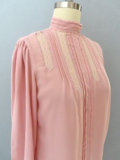 Vintage prairie blouse from the 80's era! Soft pink with pleats and see thru vertical lace insets, pleated mock collar and puffed shoulders. Buttondown back with double button cuffs. This amazing blouse would look great dressed up or casual with jeans. Estimated to fit like a modern size small-medium. Please double-check the measurements:. MEASUREMENTS--Taken with garment laying flat, in inches, doubled: Bust: 36"  Waist: 38"   Shoulder: 13" Neck: 13" Sleeve: 21"  Length: 22.5" {collar to bottom hem} Label/ Era: Casual Corner / 1980 Fabric: Polyester, acrylic buttons Stated Size: 5 Made in Hong Kong Condition: Great vintage condition. Freshly laundered. No issues. ★ The "fits like" size is just an estimate, and vintage sizing can vary from modern sizing. Please use measurements to ensure p Prairie Blouse, Cottagecore Blouse, Romantic Blouses, Pink Sheer, Lace Inset, Pink Blouse, Pink Lace, Soft Pink, Womens Clothing Tops