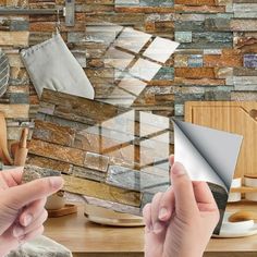 two hands are holding an object in front of a wall made out of stone tiles