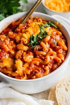 a white bowl filled with macaroni and cheese on top of a table next to bread