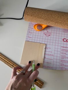 a person holding a pair of scissors on top of a piece of paper next to a cork board