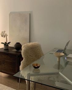 a glass table with a laptop on top of it next to a vase and plant