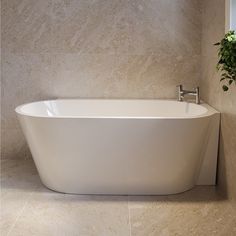 a white bath tub sitting in a bathroom next to a plant on the side of it