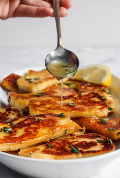 someone is dipping sauce on some food in a white bowl with lemon wedges and parsley