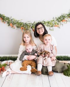 a woman and two children sitting on the floor with carrot garlands behind them in front of a white wall