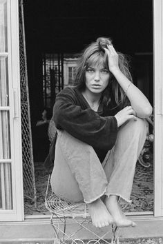 black and white photograph of a woman sitting on a chair in front of an open door