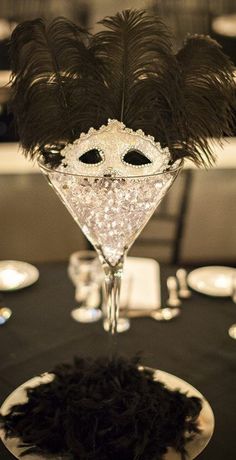 a black table topped with a martini glass filled with an ostrich feather mask