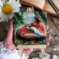 a painting of a red fox sitting on top of a wooden easel next to flowers