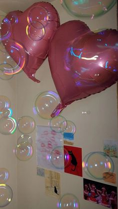 two heart shaped balloons floating in the air next to pictures and posters on a wall