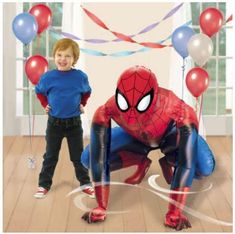 a young boy standing in front of a spider man balloon arch with balloons and streamers