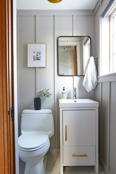 a white toilet sitting next to a sink in a bathroom under a mirror and light fixture