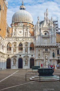 an old building with a fountain in front of it and people walking around the courtyard