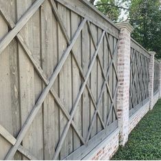 an old wooden fence that is next to a brick wall and green grass on the ground