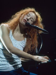 a woman with long red hair is playing the piano and singing into a microphone on stage