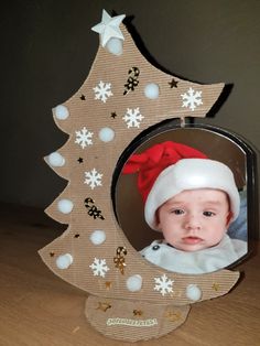 a baby wearing a santa hat in front of a christmas tree shaped photo frame with snowflakes on it