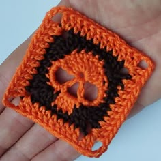 an orange and black crochet square is held in someone's hand