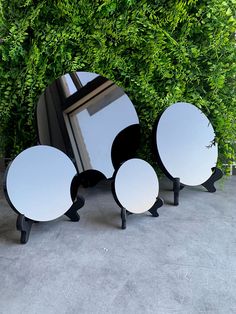 three mirrors sitting next to each other on top of a cement floor near green plants