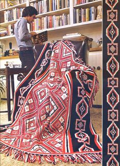 a woman standing in front of a bookshelf next to a red and black blanket