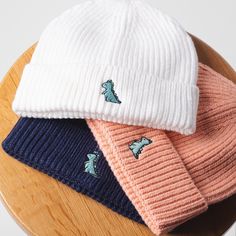 three knit hats sitting on top of a wooden table next to a white and blue hat