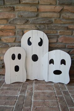 three wooden ghost faces sitting next to each other on a brick floor in front of a stone wall