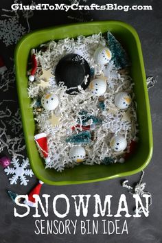 a green tray filled with snowman and other christmas decorations on top of white shredded paper