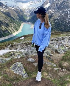 a woman standing on top of a mountain looking down at the valley and lake below