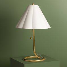 a gold lamp with a white shade sitting on top of a green table next to a wall