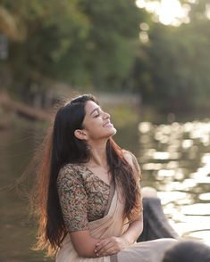 a woman sitting on the edge of a body of water with her arms folded out