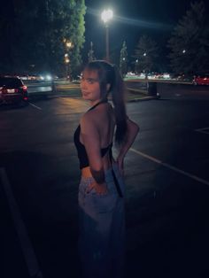 a woman standing in a parking lot at night with her back turned to the camera