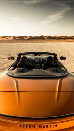 an orange sports car parked in the middle of a desert area with sand dunes behind it