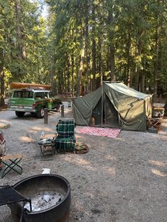 there is a tent set up in the woods next to a campfire and chairs