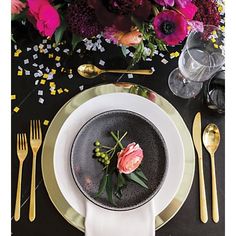 a black plate topped with flowers next to gold forks and spoons on top of a table