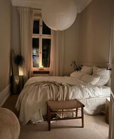 a white bed sitting next to a window in a room with beige walls and carpet