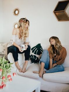 two women are sitting on a couch and one is holding a cup in her hand