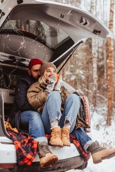 a man and woman sitting on the back of a car in the snow with their dog