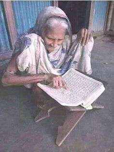 an old woman sitting on the ground reading a book